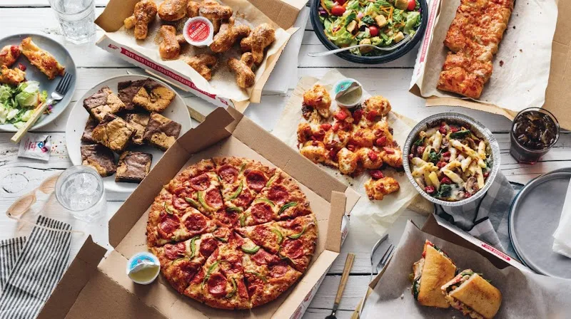 Domino's pizza spread with wings, brownies, salad, pasta, and sandwiches on table.