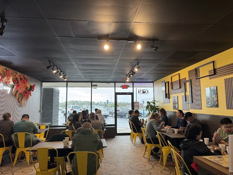 Busy Asian restaurant interior with yellow chairs, diners eating, and dragon wall decor.